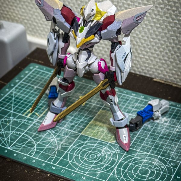 〈設定〉オーブ特別嚮導派遣技術部（通称「特派」）が世界平和機構コンパスと共同開発した試作機動兵器。格闘機であるコンパスのイモータルジャスティスをベースとし、地上での運用を想定した「ランドスピナー」や超振動ロングソード「MVS」、高性能新型センサー「ファクトスフィア」を装備している。ヴォワチュールリミュエールを応用した高機動ユニット「エナジーウィング」が搭載予定である。本機はロールアウト直前の為、1部フェイズシフト装甲の電圧調整がされていない。未完成である。（3枚目）