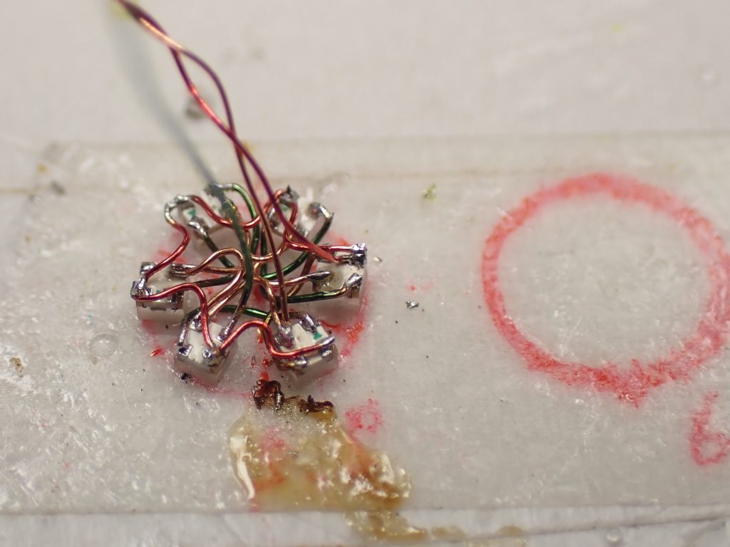 5.5mmの円を描いて6分割し、そこに1ミリ角のフルカラーLEDチップを配して配線し、これをバインダーの中に仕込んでマイコン制御で回転変色表現を演出しています。