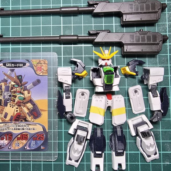 前作に引き続きガンダムコンバットネタです。DXの陸戦型的な機体を目指して胸部を３分割にしてプラ板を挟んだり等全体的にボリュームアップ！脚部は試行錯誤しながらまだまだ盛っていきたいです。キャノン砲はバルバトス用滑空砲×2ライフルはジャンクストックからDX用にと温存していたエルドラドートレスのマルチプルバレルライフルを使用方向性はこんな感じで行こうかなと・・・今回もカードイラスト1枚しか資料ないですが(泣)頑張ります。  （2枚目）