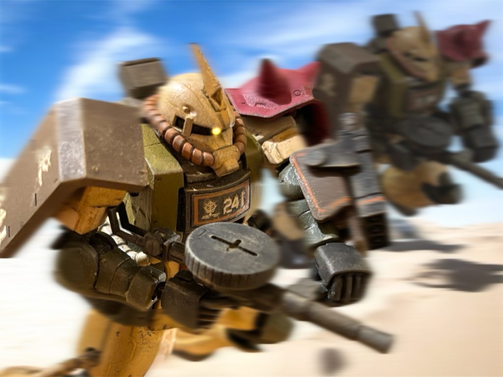 　少佐が愛機のザクを走らせる。砂漠戦仕様に特別に強化された機体だ。脚部に増設されたバーニアで、一歩のストロークを大きく取ることができる。ドムのホバーとは違うが、足場の悪い砂漠でもスイスイと飛ぶように走る。おまけに、巻きあげた砂塵が目眩しにもなる。　少佐の機体に、３機が追随する。敵機からマシンガンの火線が伸びる。次いで、轟音と共に滑腔砲の弾丸が飛んでくる。４機は砂地の上でも軽快に立ち回り、横にステップしながら砲撃をかいくぐる。