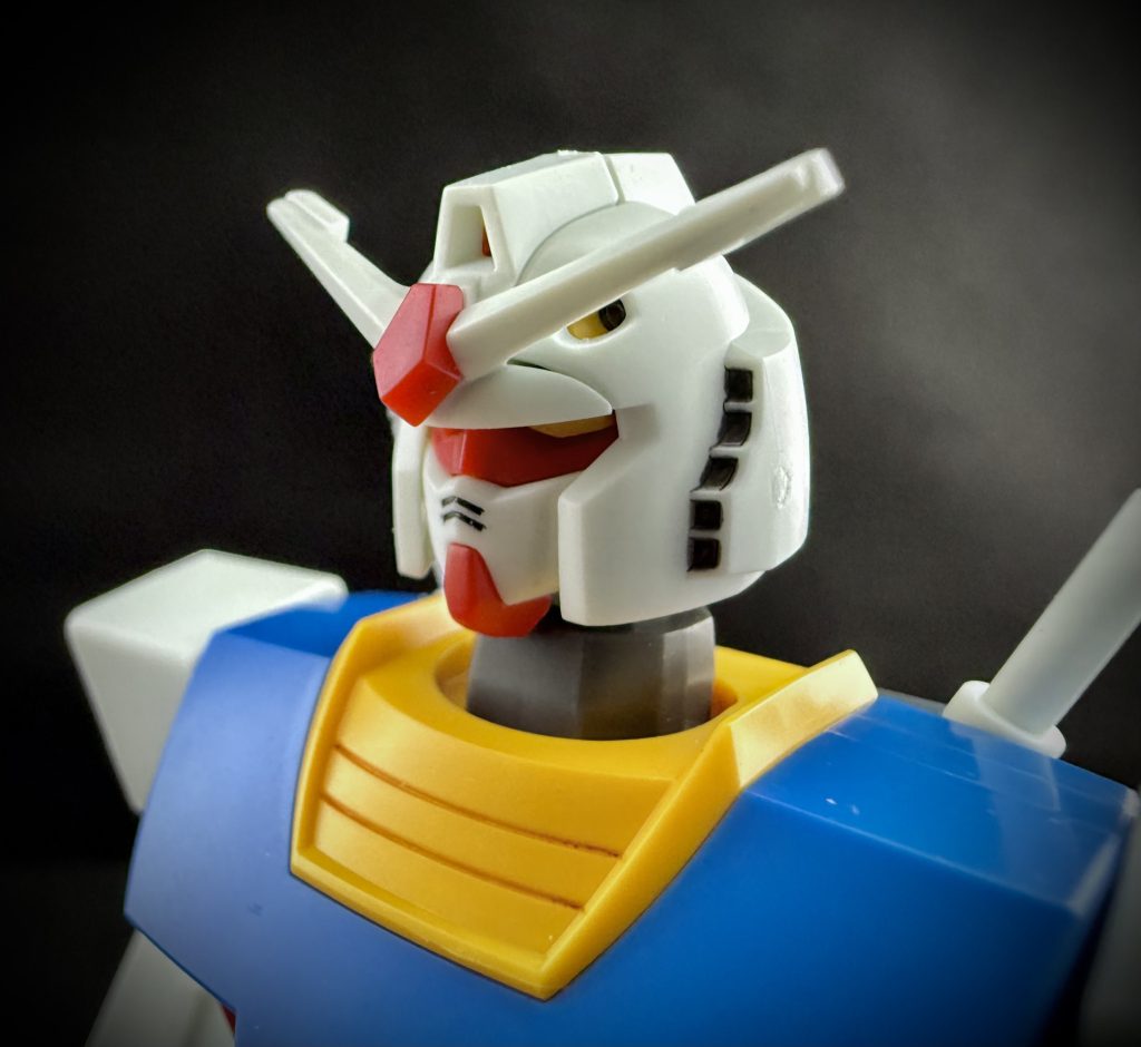 RX-78「ガンダム」このMSの特徴の一つとして、その頭部のデザインがある。ジオン公国のMS。MS-06の無機質な一つ目に対し、このRX-78の頭部は、何処か人間を思わせる、二つの目、デュエルアイを持つ、そして、その額にV字の意匠を持つ、ツノのようなアンテナ、ブレードアンテナが装着されている。…この、鋭く尖ったブレードアンテナが、無情にも耐熱フィルムを破ったのだ。 しかし、男は分かっていた。まるでスローモーションのように、破れた耐熱フィルムがRX-78の足元に落ちていくのを見ながら、自ら先になり、この耐熱フィルムを開発してきた。長く辛い日々を思い出す。予想は、していたのだ。フィルムを使おうと思った時に、RX-78の仕様書を読んだ時に。 思いがけず男に与えられた試練。もう何度頭を抱えてきただろう。しかし、男は諦めなかった。RX-78は完成した。男達は完成させたのだ。MSを単体で大気圏に突入させることのできるシステムを。男は奮起する。…ここで、ここで負けてなるものか。 もう、その場にいた誰もが男の案を待っていた。皆の期待を一身に背負い、男が打ち出した案。それは…。 「カバー」を付ける。 シンプル。余りにシンプル。鋭く尖ったブレードアンテナの先端にカバーを被せたのだ。後に、「フラッグ」と呼ばれることとなるカバーは、ブレードアンテナのデザインを邪魔しないよう、樹脂素材により成形され装着された。成形の容易な樹脂素材を使用することで、様々な形状のアンテナにそのデザインを変えることなく、装着することが出来たのだ。男の提案は、瞬く間に採用され、中にはアンテナの先端を、最初からカバーが付いたように成形されたモデルも生産されたほどであった。 …プロジェクトアールエックス