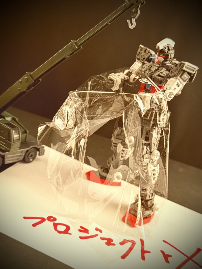 ※画像は再現映像 素材は決まった。 高い耐熱性能を持ち、薄く、それでいて頑丈なラップフィルム。これを機体に被せ、大気圏突入時の大気との摩擦に抵抗。突入後はそのまま使い捨て。 …果たして、この案は、連邦軍上層部に採用された。湧き立つ、担当部署の面々。その中に、男の姿もあった。…男は思い出す。あの夜のことを、残業を終え、家に帰ったスタッフらを呼び戻し、何事かと目を剥く彼らの前に、手に持ったラップの箱を突き付けた時のことを。「これを使う」と言った時の、スタッフ達の顔が忘れられない。疲れ果てた顔に、見る見るうちに、力が、目に光が宿るのを…。 しかし、湧き上がった彼らに再び試練が訪れる。「何処」に収納するのか?収納するとして「どの様に」収納するのか?…男達は、再び頭を抱えた。 …プロジェクトアールエックス