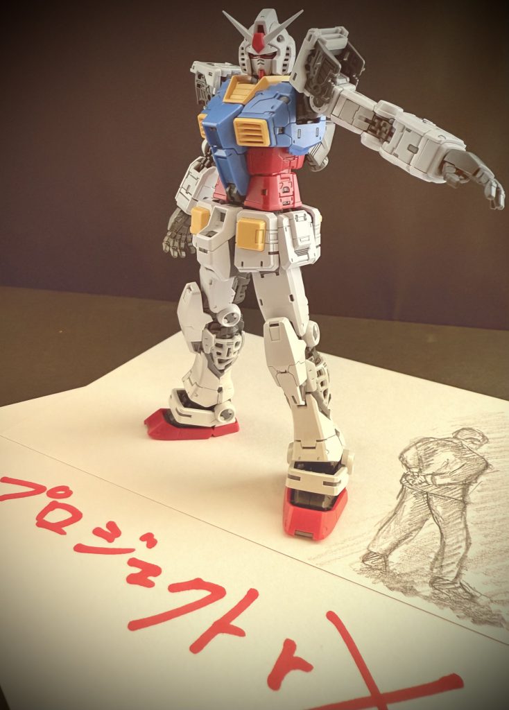 ※画像は再現映像 男は悩んでいた。 MSという18メートルの巨体。それを単体で大気圏突入させるという、軍上層部の要求。それは、自分達を含め、多くの部署に、技師達に、厚い雲を降ろしている。大気圏への単体突入。それは、機体全てに、その機体を操縦するパイロットに対しても、大きな影響を与えるのだ。…そんな軍上層部からの無茶振りとも言える要求に、多くの部署が、技師達が、頭を抱えていた。…男もその一人だ。 V計画内において、様々な部署がある。MSという巨大な工業品である以上、数えきれないほどの、ハード面、ソフト面の集合体として完成する。その中において男の担当する部署は、内装。または、梱包を主とする。人によっては、閑職。とも言える部署だ。…しかし、男はこの仕事に誇りを持っている。例えば、パイロットが座るコクピットシート。パイロットとMSの接点とも言えるシート。戦闘が長引けば、長時間座っている事になるだろう。パイロットに戦闘以外のストレスを与えないよう、様々な工夫を凝らす。男はその仕事に誇りを持っていた。だが、男にとって、全ての部署、技師らに与えられた、過去に例の無い、MS単体での大気圏突入という問題は大きかった。 大気圏へ突入する物体が、シンプルな形状であるならば、いくらでも案はあったのだろう。おそらく全ての部署を巻き込んでの大事には、ならなかっただろう。だが、MSは違う。「人型」なのだ…。機体の装甲表面に耐熱タイルを貼り付ける。と言う案も聞いた。だが、それでは駄目なのだ。人型である以上、人型である為に、そのまま大気圏突入するという事は、必ずどこかの時点で空気抵抗の問題が発生する。ましてや、大気圏への突入なのだ。大気との摩擦の問題は、熱の問題も含め、必ず克服しなければならない問題なのだ。 …そんな中、男が出した、提案。…それは、MSに、RX-78に「マント」を纏わせる。という案。MS用の耐熱性能のある外套を作る。というものだった。これならば、重量の問題、装着時においての機動性の確保、艦艇に搭載する際の様々な問題にも対処できる。しかし、自信を持って提案した男に対する軍上層部の返答。それは、「現実的では無い」…その、一言のみであった。 男達の苦悩をよそに、RX-78は完成していく。 だが、屹立する18メートルの巨体を日々、見上げる男はわかっていた。方向性は間違えてはいない。と…。 …プロジェクトアールエックス