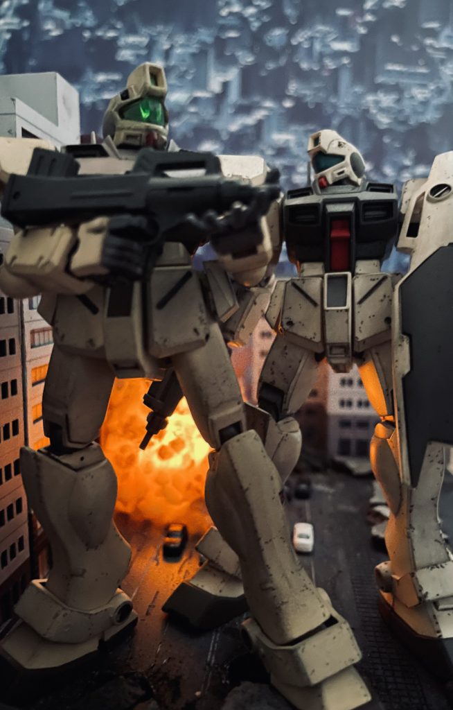 続いてMGジムコマンドのボックスアートとなります。コロニー壁面を背景に2体が並ぶ構図です。お気づきかもしれませんが新旧キットの揃い踏みです。イラストの雰囲気に近づけるため脚部を中心に強めにチッピングを施しました。