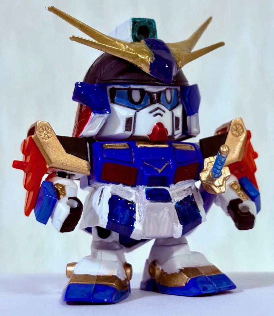 「試し斬りで終わらせてくれるなよ・・・！」武者トリスタンは「SD戦国伝～黄昏の章～」の主人公。4代目大将軍の息子で、天下泰平の時代に生まれた天宮（アーク）の若武者。剣の修行に励む傍ら、世間を知るために自ら素浪人「刃亜那無（バーナム）」または「玖按鍛笛瑠喪（クァンタン・フェルモ）」という偽名で活動し、名を揚げていくと有名な領主「写琉無彫須頭（シャルンホルスト）」の目に留まり彼の傭兵軍団のリーダーとして雇われた。好戦的でサディストな性格だが、仲間を心配したり引き際をわきまえていたりするなど根っこの部分は父親と同じく優しい心の持ち主だ。ちなみに双子の弟（妹？）がいるらしい。傭兵の活動を終えると、正式に5代目大将軍となったらしい。荒鬼頑駄無の先祖とされている。こんな感じのキャラ設定を当時付けた気がするな。てか「黄昏の章」ってまんまトワイライトアクシズじゃねーか(zaku-kao2)