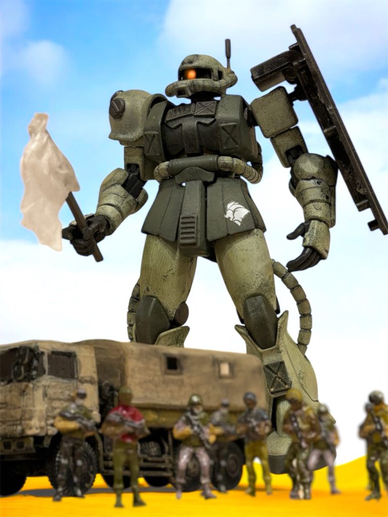 『待ってください、MSの機影が見えます。』声色に、緊張が混じる。『ザクです。１機です。』全隊に緊張が走る。『たった１機だと？それとも例のゲリラ戦法か？』こういう時に、冷静なのはイギーの良いところだ。　ディーン中尉による敵襲の報告を受け、ダマスカスへの出発を半日遅らせた。制圧済みのダマスカスからも、掩護のための戦力を差し向けている。敵もさすがにそれくらいの動きは予見すると踏んでいたが、まさかまだ粘っているなどと、誰も思わなかった。「同じ柳の下の鰻を狙う馬鹿か、それともそれだけ自分たちの作戦に自信があるのか……」『どっちでもいい。全機、とにかく足元に気を付けろ。』報告にあった潜砂からの奇襲を警戒し、イギーが友軍に通信を送る。『ヘント、ミヤギ曹長にスプレーミサイルを蒔かせろ。』『待ってください。』イギーからの通信を遮るように、再び、ミヤギからの通信が入る。どこか、言葉がたどたどしい。『何も、武装していません。白旗、を、掲げています。』