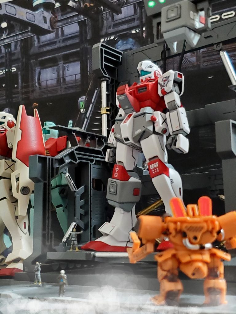 宇宙世紀0079年12月下旬、連邦軍は宇宙要塞ソロモンを陥落させた事によりジオン侵攻の足掛かりを得た🎵そしてソロモンからコンペイトウへ改名された要塞へ輸送艦隊により補充物質が搬入される🚢ソロモン攻略戦の際に愛機であったジムスナイパーカスタムが中破したユング少佐のもとにも新たな機体、試作型ジムコマンド２号機が配備された👍️RX-78に近い性能を目指したこの機体には試験部隊によるG-3の実働データをもとにマグネットコーティング技術や最新バージョンのOSを導入🔧高いスペックを誇る機体に仕上がっていた😊そして試作型２号機には『G-Ⅳ計画』と呼ばれる極秘MS開発で得られたノウハウを生かした装備パックを用意❗パック内容は最新のビームライフル、シールド、腕部ガトリングパック✨対弾性強化のチョバムアーマーパーツなど火力と装甲強化をテーマとした強化パーツ一式である😔✨コンペイトウMSハンガーにてG-Ⅳパックの換装作業を行う試作型２号機🤩🎵連邦軍は確実な勝利を得るため、戦線に惜しみ無く戦力を投入していく😎左肩にはパーソナルエンブレムである『シュモクザメ🦈』も描かれ、ユング少佐は満足して機体を見上げていた…😌🎶