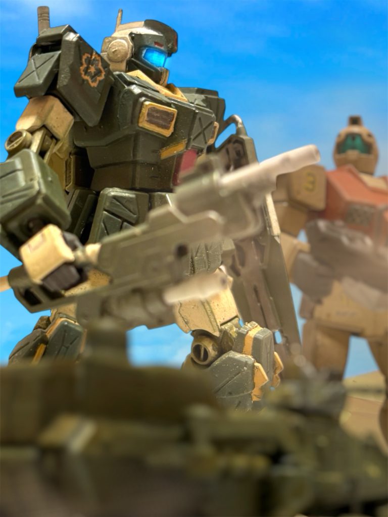 「逃がしたか。」 気骨のあるやつだった、とイギーは思った。最後にもらった一撃は、ウェラブルアーマーが炸裂したおかげでカウンターに持ち込めたが、通常仕様のジムならあのまま押し切られていただろう。あの思い切りの良さは、どこか、オデッサで最後に会敵したザクを思い出させた。 進出していた敵MS隊は、友軍が掃討したらしい。手ごわかったのは、逃げられたグフと、そいつを庇うように立ち回っていたザクくらいだったようだ。おそらく、あと数時間としないうちに、この戦線は落ち着く。あとは何日か掛けて、サラサールを包囲して締め上げるのだろう。「ヘント少尉とミヤギ曹長はどうした。予定の攻撃地点に合流したのか。」 後から追いついて来たホバートラックに通信を送る。『いえ、随伴していた中隊のみ到着して、攻撃に参加しています。機数と編成が若干変わっているようですが、どちらも、2番機が指揮を引き継いだそうです。』「何をやってるんだ、あいつらは。決戦場で駆け落ちか、恋愛脳が。」『いえ、報告によると、進軍の途中でミヤギ曹長の隊が敵の奇襲を受けたようです。例の、砂にもぐるザクの部隊です。』 ミヤギのキャノンは”シングルモルト”で目立ちすぎた。敵の恨みも買っていたことだろう。敵がそちらに戦力を差し向けるのは、確かに納得できた。『”血濡れの左腕”も増援で合流したため、2人で防いで、中隊を先に向かわせたようです。』「あいつ、また撃墜されていないだろうな。」 味方を恐れさせた”血濡れの左腕”。あのグフは、オデッサでヘントのガンダムを撃墜したやつだろうと、イギーは半ば確信していた。「ここの戦線は落ち着くはずだ。俺たちは一度後退して、ヘント少尉とミヤギ曹長を捜索に行くぞ。」 イギーは中隊に命じる。つい数日前に、こんなことがあったな、とイギーは思った。「どうせ、どっちかが墜とされて、また砂漠の真ん中でいちゃついてるんだろう。ゆっくり行くぞ。」~~~~~~~~~~~~~~~