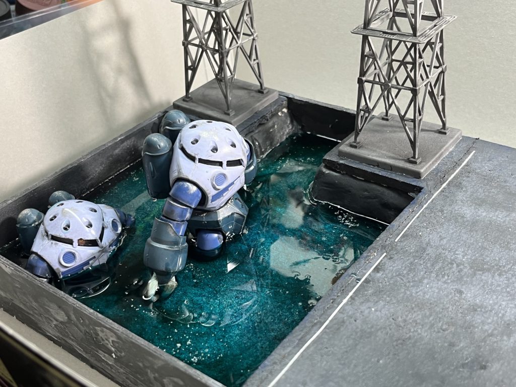 前回ザクⅡジオラマでレジンで大失敗した反省を活かし、アクリル板でレジンを塞き止め、隙間の穴埋めにはシリコンをしっかり塗り固めました。今回の失敗点はレジンの硬化です…樹脂の比率が悪かったのか、均一に混ざってなかったのかはわかりませんが、表面が上手く固まらずプルプルしてやがります。今回のジオラマ、水面に大量のレジンを使用しており、これ以上レジンを購入するのも嫌になっちゃってモチベーションが完全に低下しちゃいました…。もう一度上からレジンを乗せればリペアはできそうですがもうレジンが怖くてしばらくはいいかなってなっちゃってます。今も部屋の隅でプルプルしてらっしゃいます。 本来はこのズゴック達の先頭に港に上陸しながら右腕でミサイルを飛ばし、左腕で辺りのコンテナを叩き潰しているハイゴッグが居る予定でした…。気が向いたらまたリベンジしたいですね。