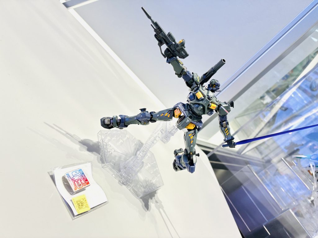 現在、こちらの作品は近所のガンダムベースにて展示いただいております。ガンダムベースでは、ガンプラ45周年を記念して「45周年記念コンペティション」が開催されており、こちらのコンペで展示させてもらいました。展示の際の審査に通り、指定の条件をクリアすると記念品である「45周年限定ピンバッジ」を頂けるという事で今回参加に踏み切りました。