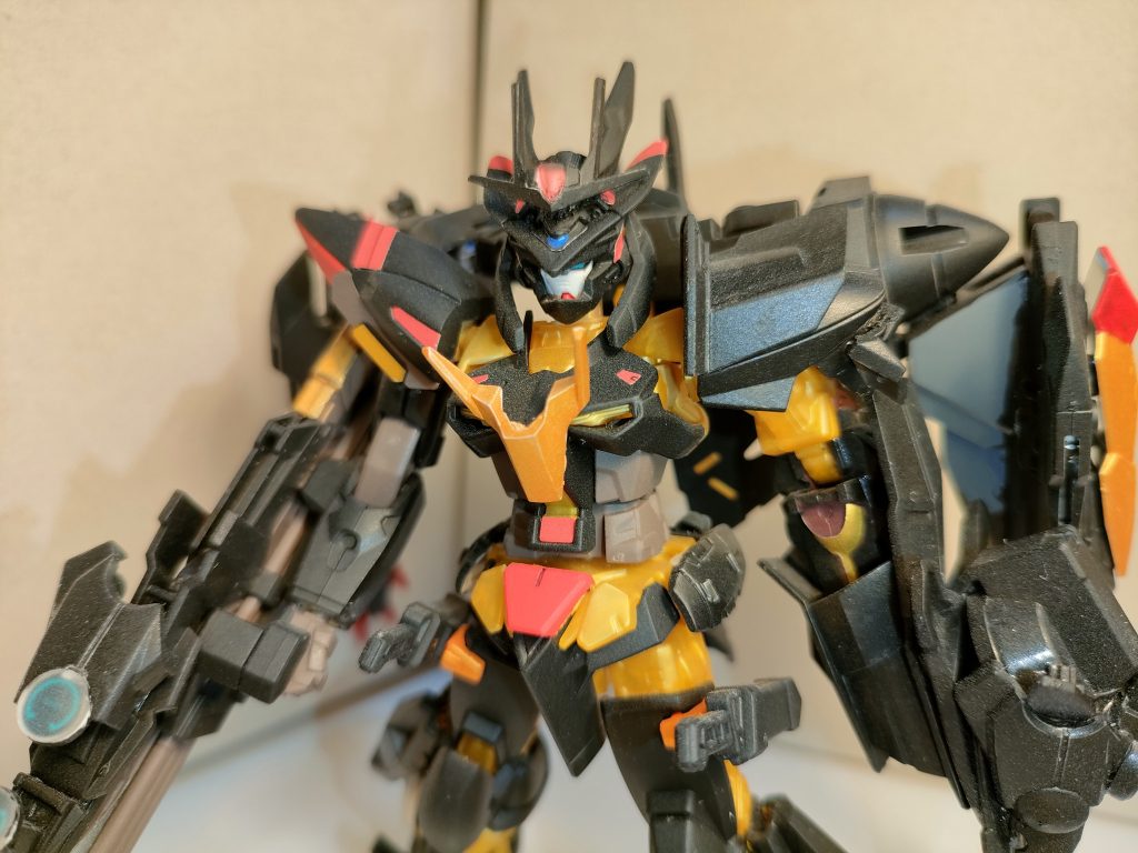 何処からか流れ付いた、モビルスーツの残骸を回収したと言われているが、その状態は非常に奇妙奇天烈な形状をしていた。「 例えるなら…金属に侵食されたような…?機体から鉄が生えたような感じだな…」 それでも、内部のデータは解析回収できたてらしく、所々は既存の技術が使われていたがこの世界とは微妙に異なっているらしく、特に動力源部分は明らかに未知のものだったらしい…。 さらに金属部分も見たのことないレアメタルらしく、これらの未知の技術や物質を取り入れた結果、ミラージュコロイド粒子との併用により機体装甲の防御力が上昇し、機体重量の軽減やエネルギー問題が多少改善されている。