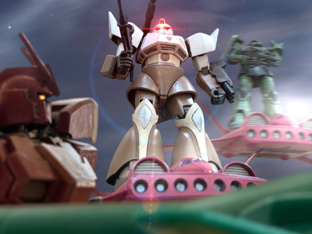 「やめろ、全機、銃を降ろせ。」 ジンは、カルアが率いてきたMS3機に、ライフルを向けた味方を制止する。カルアたちも撃ってこない。ガンペリーの横を、伴走するようにゆっくりと浮遊している。『ごめん、ジン。遅くなった。』まるで、デートの待ち合わせでもしていたかのような、浮ついた女の声が通信機に入った。『通信回線を敵に教えたのか!?』 ケーンが驚愕の声をあげる。「教えた、わけではないです。分かってしまうんだ、なあ、カルア?」『違うよ、これは、教えてくれた人がいる。』 突如明かされたスパイの存在に、ジンを除いた誰も動揺する。(何だ、この戦場は……すべてが狂っている!) ケーンは吐き気を堪えながらも、なんとか操縦桿を握り直した。『で、どうするの?』「どうするって……どうしたらいい?」『考えて、なかったの?』くすくすと笑うカルアの声を、敵も味方も、オープン回線で聞く。(ふざけるな……っ!) 異常な戦場の空気を、”デューク”が斬り割く。ジムのライフルをあげ、カルアの乗る機体に銃口を向けた。しかし、その瞬間、”デューク”の視界を光が包んだ。~~~~~~~~~~~~~~~ ”デューク”のジムの銃口が、カルアの乗るゲルググに向けられる。瞬間、時間が止まる。いや、無限に引き伸ばされていく。カルアのゲルググに銃口を向ける”デューク”のジムの動きが、永遠に続くスローモーションのように見えた。(嫌だ!壊される——!?) それは声ではない。カルアの魂の叫びが、絶望の奔流となってジンの精神に流れ込む。違う、これは俺自身の叫びだ。俺の唯一の理解者が、俺の世界が、今まさに