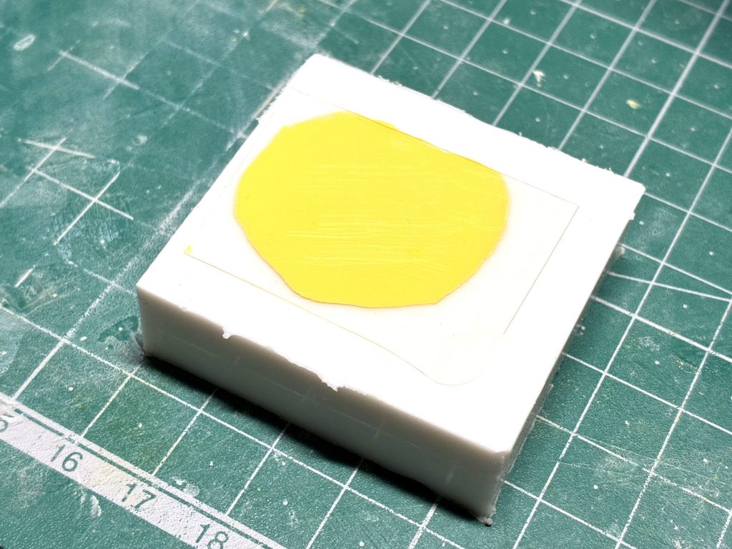 たまたま近くにあった透明なプラ板(お菓子の箱の切れ端?)を使用して気泡が入らないよう注意しながらパテを押し付けてます。