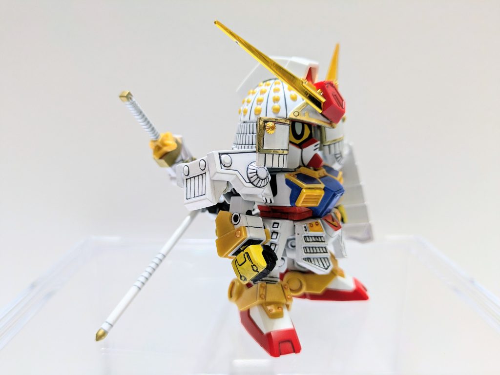 肩鎧の大袖を短くカットしてモチーフに近づけました。足の裏はパテで肉抜き埋めし、黒プラ板でカバー。黄色のパーツは成形色を活かしたかったので未塗装。胸鎧の通気口のようなパーツは『ファーストガンダム大将軍』のものを移植。兜飾りはメッキにしたかったのでそのまま使用しました。ゲート処理や合わせ目消しも部分的に行いましたが技術的にまだまだ。また、ミニ磁石を全身にいくつも埋め込んでいます。兜飾りや肩鎧、盾は磁石でくっついています。モロ見え、死角が雑など反省点多し!