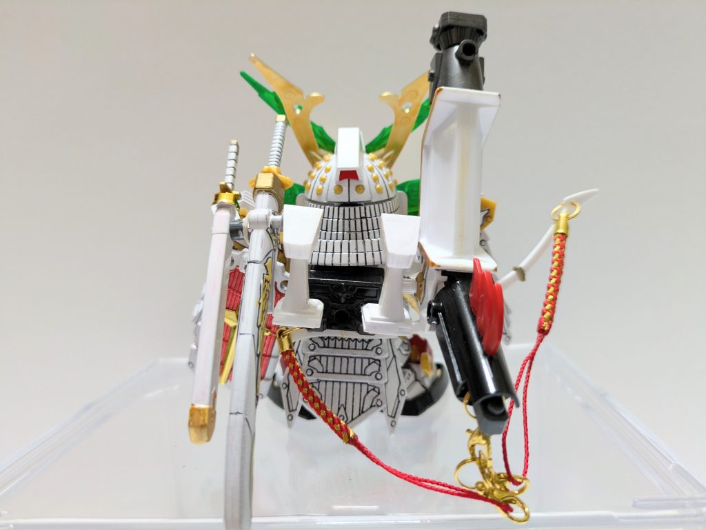 バックパックはこの形態のために拡張しています。右手側にファーストガンダム大将軍の大目牙バズーカ、左手側に武輝丸と武久丸を装着できるようにしました。また、右腕には改造討魔弓を装着。盾と同じように白鋼メッキのパーツを赤く着色さしてミキシングしたものです。腰とは色の違う綱飾りを大目牙バズーカに繋ぐ形であしらっています。反省点としては肩鎧の大袖が干渉して討魔弓と盾が腕の横で装着できず、背面に回ってしまったことです。