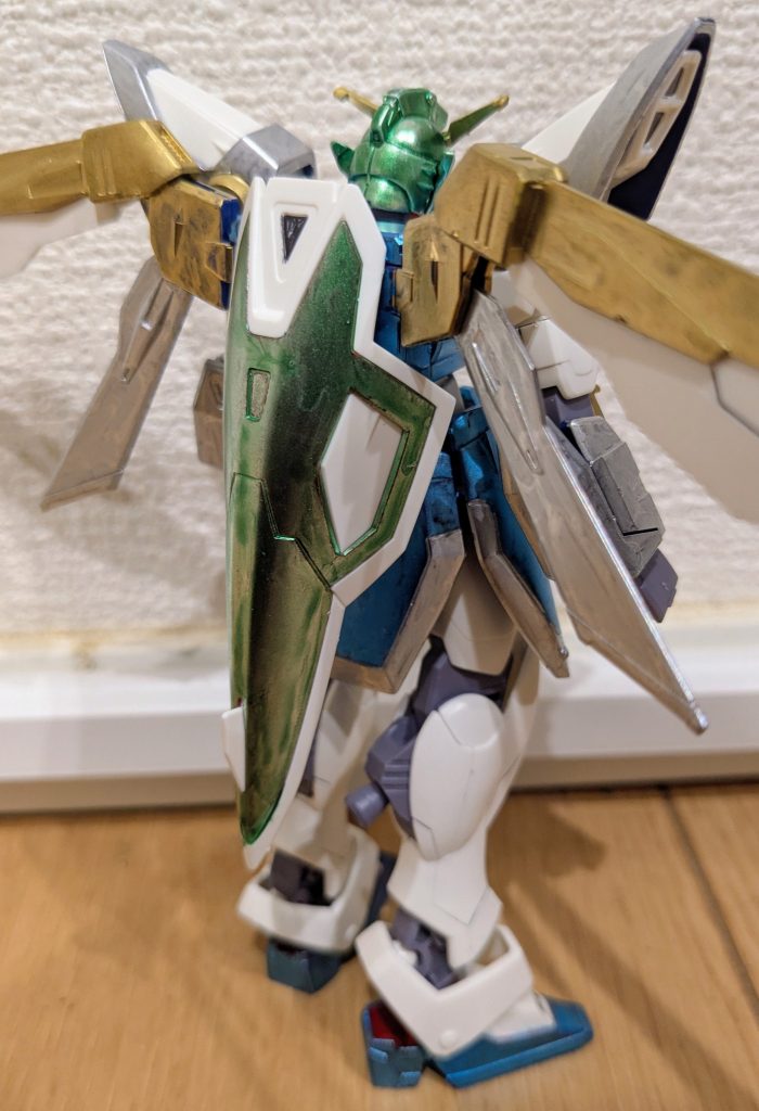 バックショットから１枚。色レシピは以下の通りです。アンテナは中央部含め、リボンをイメージしてゴールド。頭はフェイス以外を、髪をイメージしてメタリックイエローグリーン。シールドはバックパックに下向きに接続し、赤だった部分をメタリックイエローグリーンに塗装し、大妖精のおさげイメージにしてみました。本体色とスリッパ部分は、彼女のワンピースと靴をイメージしてメタリックブルー、スカートの模様をイメージして、スカート先端はシルバーにしました。ウイングは赤の部分をシルバーに、付け根部分をゴールドに変更。腕、肩の青部分はすべて彼女のシャツのイメージでシルバーに変更です。 