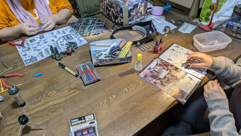 作品名：Mioガンプラ会、深夜にまで及ぶ🤣<p>今日もキャンプ場内の古民家でガンプラ会が開かれておりました。女性お二人が粘りに粘って深夜1時現在でもまだ製作を続けております😳✨凄い‼️ 一人はRGのズゴック、もう一人はHGザクIIのルショーン機👍🏽</p>
