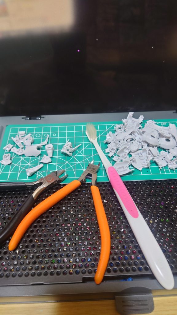 パーツ切り出し。二度切りが基本。使っている道具は・プラモ向上委員会 ワークステーションVer2.0 ～ 作業台。昔はティッシュを敷いてゲートを落としてた。使ってみたらニッパー置きとかあって超便利だった・タミヤ クラフトニッパー ～ ランナーからの切り出し用。真鍮線ぶった切ったり、極太クリアランナーゲートぶった切ったりと滅茶苦茶酷使してる最古参・ゴッドハンド ブレードワンニッパーL ～ 二度切り用。本当はアルティメットニッパーが欲しかったけど、自分は左利きで使いにくいことと当時は左用アルティメットが販売前だったのでこれ買った。アルティより雑に使える分、こっちの方がいいかも・歯ブラシ ～ 雑多に使えて想定以上に活躍する、適当に買った100円もしないやつ