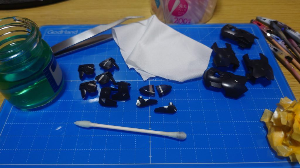 今回は一部を水性塗料で塗り分け。水性塗料をエアブラシで吹くときはエア圧を「1.2MPa」くらいにして、パーツとエアブラシの距離をかなり離し気味にしてうっすら砂吹き、5分くらい乾燥させます。それからキッチリ色を乗せて15分～30分くらい乾燥させますこの水性塗分けの時のマスキングは大雑把で大丈夫です。水性塗料はキッチンマジックリンで拭い落すことができるのです！中央の肩パーツとフロントスカートをご覧ください。左はザックリマスキングで塗装した状態、右はマジックリンで拭き取り後。キレイに拭き取れますマジックリンは適当なスペアボトル(画像はクレオス製)に入れ、綿棒で拭き取ります。吹いた後はマジックリンでやや濡れているので布で拭いて綺麗にしています。ティッシュだと繊維が付着することがあるので布推奨です。画像の布は・プラモ向上委員会 ダストエンドクロスプレミアム