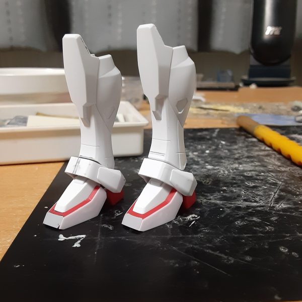 バルバトスの肉抜きを埋めようとしたらエポキシパテが余ったので、0ガンダムの脚やシールドに使う事に。で、そのままの流れで0ガンダムの製作に突入。 良くない兆候だけど、バルバトスの方はシリンダーをあと一本作ればいいだけだからすぐ終わるはず。いいんだいいんだ、これは浮気じゃないんだ！ この0ガンダム、キットではスマートな体型で、特に脚部は腿が短く脛がかなり長いガンダムフレーム(うわああぁ!)のようなバランスになっています。一方劇中では頭身がそこまで高くなく、ムキムキな太腿をしていて、キットとは全然違う体形。なので自分にできる範囲で「細さ」を打ち消すような改造をしてみます。 まず足首を裏打ち後に正面で1.5mm短縮。左右から0.3mmプラ板でサンド。少しでも太く見せるため、C面を無くしています。 関節ブロックを上下に3mm短縮、アンクルアーマーを中央で1mm幅増し。そのままではアーマーを付けられないので脛下端のPCにかぶせるような形のブロックをプラ板から自作し、アーマー裏とBJで接続。強度が足りないのでこの段落に書かれている部分だけで0.3～0.5mmの真鍮線を７本も使っています。 脛は側面中央のエッジを起点に、正面のみを斜めに2.5mm短縮。BJとの干渉で脛を前に倒す方向へはほとんど動かなくなりましたが、横への可動範囲はほぼ変化なし。 これらの工作で脛や足首がいくらか太く、短く見えるようになったはずです。高さが2mm弱低くなったので、その分は腿を伸ばしてバランスをとる予定。（3枚目）
