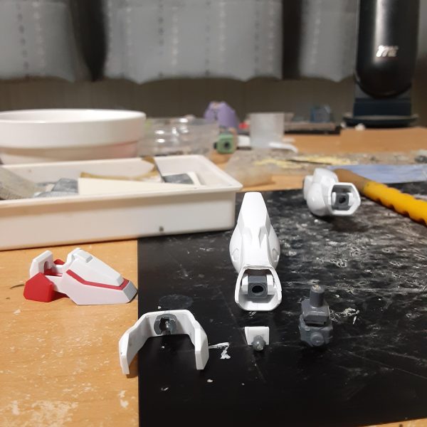 バルバトスの肉抜きを埋めようとしたらエポキシパテが余ったので、0ガンダムの脚やシールドに使う事に。で、そのままの流れで0ガンダムの製作に突入。 良くない兆候だけど、バルバトスの方はシリンダーをあと一本作ればいいだけだからすぐ終わるはず。いいんだいいんだ、これは浮気じゃないんだ！ この0ガンダム、キットではスマートな体型で、特に脚部は腿が短く脛がかなり長いガンダムフレーム(うわああぁ!)のようなバランスになっています。一方劇中では頭身がそこまで高くなく、ムキムキな太腿をしていて、キットとは全然違う体形。なので自分にできる範囲で「細さ」を打ち消すような改造をしてみます。 まず足首を裏打ち後に正面で1.5mm短縮。左右から0.3mmプラ板でサンド。少しでも太く見せるため、C面を無くしています。 関節ブロックを上下に3mm短縮、アンクルアーマーを中央で1mm幅増し。そのままではアーマーを付けられないので脛下端のPCにかぶせるような形のブロックをプラ板から自作し、アーマー裏とBJで接続。強度が足りないのでこの段落に書かれている部分だけで0.3～0.5mmの真鍮線を７本も使っています。 脛は側面中央のエッジを起点に、正面のみを斜めに2.5mm短縮。BJとの干渉で脛を前に倒す方向へはほとんど動かなくなりましたが、横への可動範囲はほぼ変化なし。 これらの工作で脛や足首がいくらか太く、短く見えるようになったはずです。高さが2mm弱低くなったので、その分は腿を伸ばしてバランスをとる予定。（2枚目）