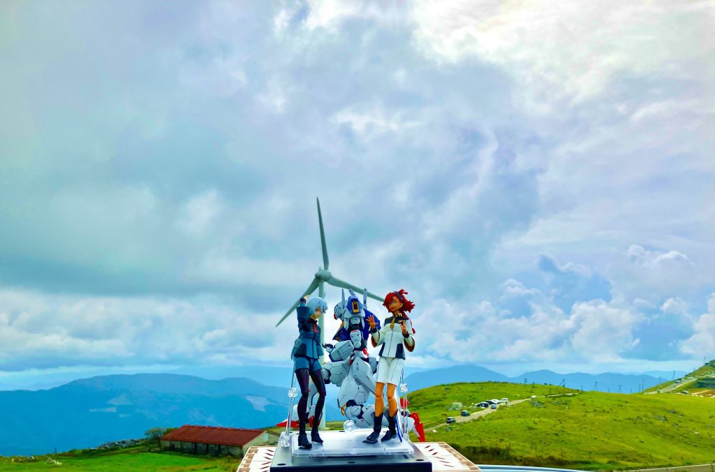 ここのロケ地は愛媛県と高知県の県境に跨がる『四国カルスト』です。日本三大カルストの1つであり、標高約1,400mのこの高原は360度のパノラマ絶景ドライブコースとして有名です。なので、四国の屋根と表される場所なだけに天候がすぐ変わるとのことでしたが、当日は曇ってはいたものの運良く雨は降ってませんでした。その為当初はエアリアルだけ撮る予定だったのが、雲と太陽の加減が良い感じに映えてたので、水星の魔女第1話最後の『お堅いのねシーン』も急遽撮影しました。ちなみに今回はパノラマ景色や風車とのサイズ感を出す為にいつものHGではなく、フルメカニクスのエアリアルの方を買ってきて作って持参しました。1/100サイズだからそのままタッパーに入らなくて、バラバラに分解してやっと格納できた。