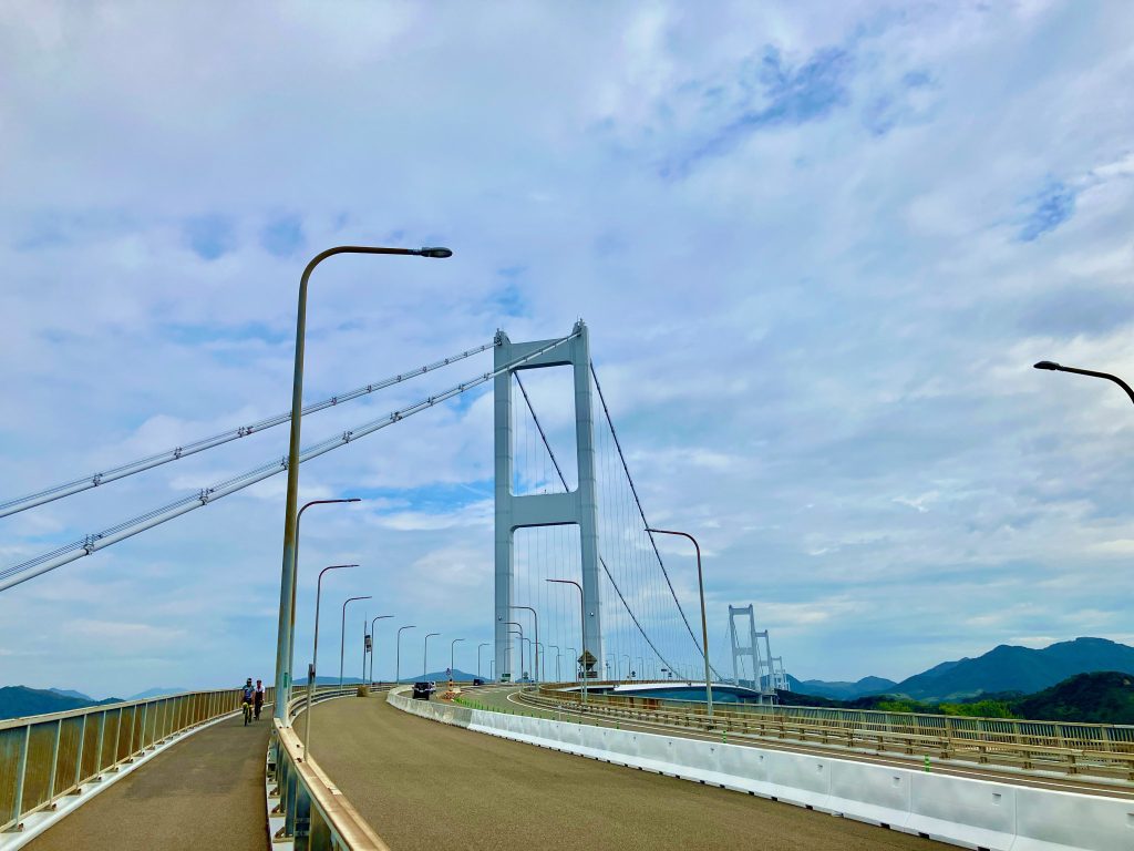 ここは日本周遊ツアー広島県・しまなみ海道の再現カットです。しかし実際には、愛媛県今治市の来島海峡大橋の方がスレミオがいた場所だったので、こちらの場所に来ました。撮影スポットは高速道路上で車を止められない橋の上だったことから、橋の麓でレンタサイクルを借りてえっちらこっちら自転車こいで向かいました。周遊ツアーのイラストの正確な場所だと橋脚から吊らされてる左右のケーブルが重なるとこなので、撮影場所のもう数十m先のとこなんですが、4本目の橋の終点が見えることまで映ってた方が奥行きがあってミオリネがへばってる感があったので少し手前にズラして撮りました。今回の小道具:スレミオのレモネードとフィギュアサイズの自転車2台を用意。しかし今回は友人の自転車もあったから画角のバランス的にフィギュア自転車は使わなかったです。