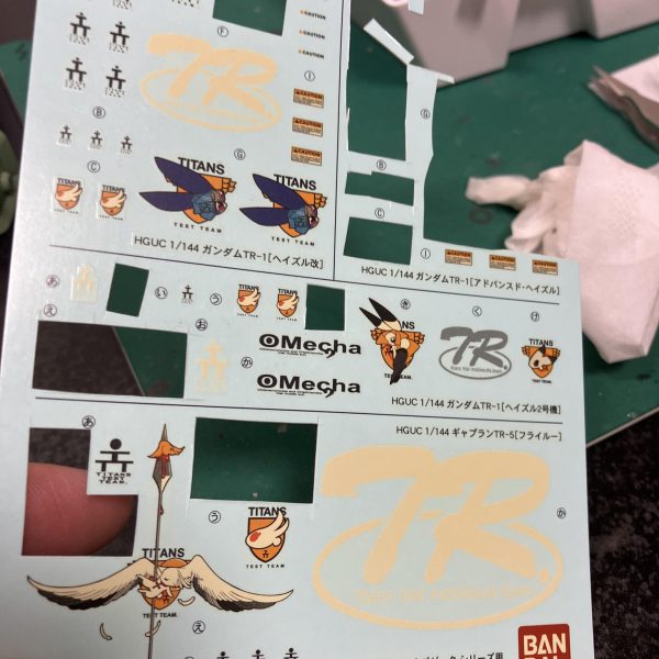 さて、ハイザックカスタム、大好物のデカールタイム、トップコート前の一手間ですね🥳というわけでディターンズはティターンズでもA.O.Zらしくテストチームの試作機としてTTTマークを使用しましょう🥰、、う〜ん、流石に初期のA.O.Zデカールは経年劣化が著しい😑特に白系はセピア化してる、、😅大判のプレバンデカールからマーキングを拝借しベースはコーションデカールですね、オレンジ&ホワイトのツートンが良さそう😉TTTとなると、指先はやっぱり赤ですね☝️🖌️使い捨て筆でホワイト下時に赤塗装、ハミ出した部分は新兵器のスミ入れ筆ペンでリタッチですね〜😬　ゴマカしやすい🥳（2枚目）