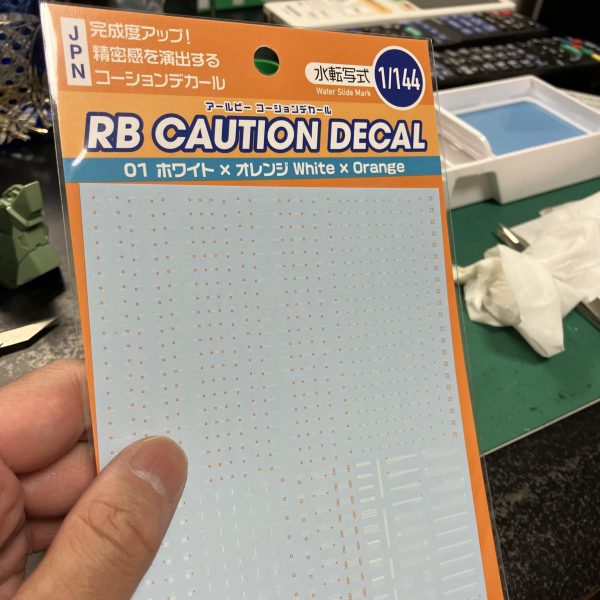 さて、ハイザックカスタム、大好物のデカールタイム、トップコート前の一手間ですね🥳というわけでディターンズはティターンズでもA.O.Zらしくテストチームの試作機としてTTTマークを使用しましょう🥰、、う〜ん、流石に初期のA.O.Zデカールは経年劣化が著しい😑特に白系はセピア化してる、、😅大判のプレバンデカールからマーキングを拝借しベースはコーションデカールですね、オレンジ&ホワイトのツートンが良さそう😉TTTとなると、指先はやっぱり赤ですね☝️🖌️使い捨て筆でホワイト下時に赤塗装、ハミ出した部分は新兵器のスミ入れ筆ペンでリタッチですね〜😬　ゴマカしやすい🥳（4枚目）
