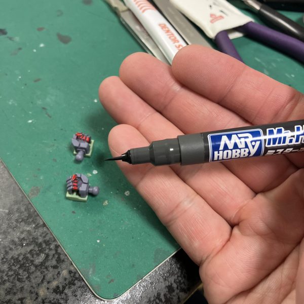 さて、ハイザックカスタム、大好物のデカールタイム、トップコート前の一手間ですね🥳というわけでディターンズはティターンズでもA.O.Zらしくテストチームの試作機としてTTTマークを使用しましょう🥰、、う〜ん、流石に初期のA.O.Zデカールは経年劣化が著しい😑特に白系はセピア化してる、、😅大判のプレバンデカールからマーキングを拝借しベースはコーションデカールですね、オレンジ&ホワイトのツートンが良さそう😉TTTとなると、指先はやっぱり赤ですね☝️🖌️使い捨て筆でホワイト下時に赤塗装、ハミ出した部分は新兵器のスミ入れ筆ペンでリタッチですね〜😬　ゴマカしやすい🥳（7枚目）