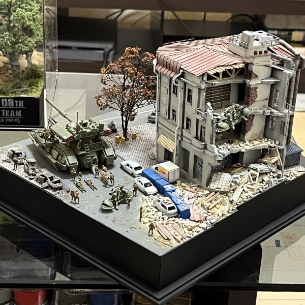 負傷兵フィギュアを追加しました。UMRCのオニー・カスガはいませんが😅よろしければ画面をタップし拡大してご覧に下さい。劇中では死傷者の描写が多くて戦争映画を観ている感じでした。あの悲壮感をガンプラで戦場ジオラマとしてしかも1/144のミニスケールで表現できてたら申し分ないと思ってます。マゼラアタックもウェザリングに手を加えました。雨垂れに埃が付着した感じで全体的に汚してます。アスファルトも少し気に入らなかったので表面をけがいてダメージを加えています。あと心残りとなっているのが建物のウクライナ語の看板です。ロケハン建物写真の正面エントランス上とオーニングテント上に取り付けられている物です（テント上のアルファベットは全く読み取れません😅）。何度となく挑戦してますがアルファベットをうまく切り抜けず挫折を繰り返してます。ミリタリースケールのジオラマだと建物の看板とか結構リアリティ出せる要素だったりするんですけど、デザインカッターで切り抜くにも1/44のサイズは小さ過ぎます😭まだ時間ありますから引き続き頑張ろうと思います。（2枚目）