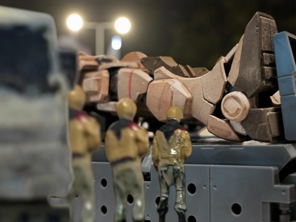 「念の為です。」 ヘントは、連邦軍の制服の上着をアーサーに渡す。アーサーがそれを羽織ると、三人は、荷台から降りた。 月明りに照らされて、サンドカラーの機体の残骸が横たわっている。「撤退するとき、空から見た。こいつは、我々の友軍機ごと、自分を撃たせていたな。」 アーサーは、青く澄んだ瞳を、苦々し気に細める。「わたしも何度か組み合ったが、パイロットはなかなか腕が良かった。あの腕ならば、生き延びて、仲間を守るべきだというのに、こいつも下らない英雄主義に溺れたのだろう。自己の死を、勝利や栄光で飾るなど……」「恐縮ですが。」 ヘントが、おずおずと口を開く。「その機体のパイロットも、わたしです。」 アーサーは思わず振り返った。「貴官は不死身か!?」「そうだ、そいつは我が隊の誇る、不死身の”被”撃墜王だ。殺しても死なない。」油断なく銃口を光らせながらも、イギーが軽口を叩く。「ついでに言うと、お前を倒したガンダムも、そいつだ。」アーサーは、その顔に動揺の色を浮かべたが、うつむき、やがて、自嘲気味に息をついた。「なんだ、まるでコミックブックか映画のような話だな……君にとっては、わたしはリベンジを果たした”宿命のライバル”というわけか。」 それなら、個人的な興味も持とうというものだ。「……そういう、ことも、ありますが……。」 ヘントは、少しためらいながら続けた。
