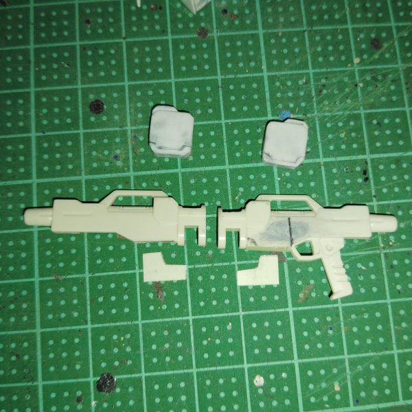 　ビームライフルのストーリー投稿第１１弾です。　今回は、前回から製作を始めた追加パーツをビームライフルに取り付けるための下準備をもう少し行います。　もともと陸戦型ビームライフルの銃身左側にあったディテールをパテで埋め、ヤスリとサンドペーパーで平坦にしていきます。　これで、銃身右側と同じくシンプルなデザインになりました。　さらに、追加パーツを取り付けた際に隙間ができないよう0,3mmのプラ板をカットし、追加パーツを取り付ける下地部分に貼り付けます。　ついでに、もともとビームライフル側面にあった四角というかいびつな六角形のディテールに付いていた小さなピン状のディテールも、デザインナイフでひとつ切り飛ばしました。　これで追加パーツを取り付ける下準備が整ったので、次回から追加パーツの仕上げをしていきたいと思います。　大方ゴールが見えてきたとはいえ、完成まではもうしばらくかかりそうですが、どうか気長に、ネタバレなしでお付き合いください。（4枚目）