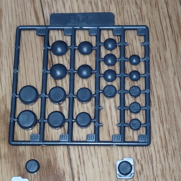 　ビームライフルのストーリー投稿第１２弾です。　今回は、前々回から開始した追加パーツの製作を進めていきます。　まずは前々回プラ板を貼り合わせておおよそ形にしたパーツの細かい隙間などを、パテを使って埋めてしまいます。　パーツ下側にカッターでスジボリを入れ、仕上げにヤスリやサンドペーパーで表面処理を行いました（このあたりの加工途中の写真を撮り忘れてしまったので、文章のみでの説明となります・・・）。　そこから今回のメインである、ディテールアップを施していきます。　まずは以前ガルバルディαを製作した際に購入した市販のディテールアップパーツから、7,0mmの円筒形パーツを切り取り、貼り付けます。　次に、以前ゾゴック（グリフォン隊）を製作したときに使用したウェーブのR・リベットから1,0mmと1,2mmのモノをチョイスし（1,2mmの少し大きめの方は、円筒形パーツ外の右上の部分です）、貼り付けました。　それにしてもこの小さいリベット、「カッターの刃の先でパーツを拾い、瞬間接着剤またはプラモデル用接着剤を少し付けます。」という、なかなかに鬼畜難易度な指示がしてあり困惑しました（まぁ確かに、ピンセットでも拾えないサイズですけどもカッターで拾えって・・・）。　さて次回ですが、実はここにきてちょっとした問題が発生してしまったので、その問題点をなんとか解決していきたいと思います。　　ようやくこの武装の完成が見えてきましたので、どうか気長に、ネタバレなしでお付き合いください。　（2枚目）