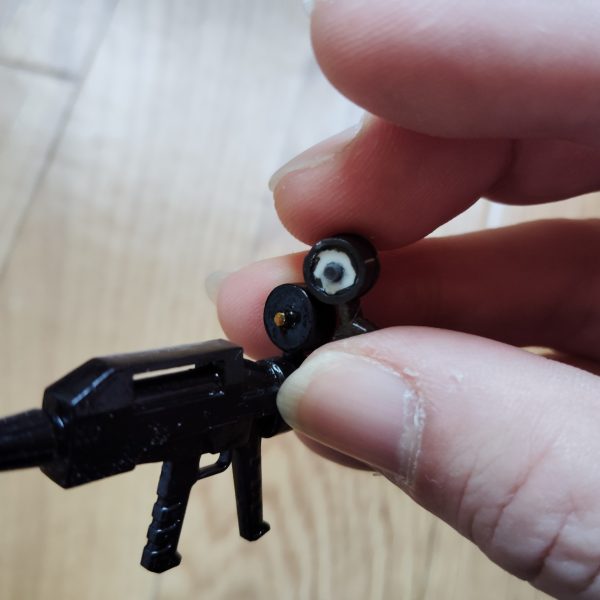 ビームライフルのストーリー投稿第16弾です。 前回、「次回はいよいよ塗装して、この新型ビームライフルを完成させたいと思います」と書きましたが、ここに来てまだ改修が必要なポイントが残っていることに気付いてしまいました・・・。 スコープの後部ですが、どう見てもガンダムのビームライフルと同型のこのスコープ、手持ちのHGUCガンダムのビームライフルと同じディテールを施そうと思っていたのをすっかり忘れたまま、塗装を進めてしまっていました。 というワケで、まずはスコープ裏側にフタとして貼ったプラ板にピンバイスで穴を開け、ディテールアップ用のパーツを差し込むことができるようにします。 そして肝心のディテールアップ用のパーツですが、ジャンクパーツの中にあったSDザクの動力パイプを、ヤスリやサンドペーパーで直径1,3mmほどになるまで削って成型しました。 そして、それを先ほど開けた穴に差し込み、パテと接着剤で固定して完成・・・となるハズでしたが、何しろ小さいパーツなので、ピンセットで挟んで接着剤を塗っている最中にパーツがどこかへ飛んでいってしまい、紛失しました・・・。 仕方なくもう一度SDザクの動力パイプからパーツを削り出し、なんとか必要なパーツを確保することができました。 今度こそ加工が完了した(よね・・・?)ので、次回は塗装を仕上げ、各部パーツを組み上げ、この新型ビームライフルを完成させたいと思います。 お待たせしてしまって申しわけありませんが、最後までネタバレ、ネタつぶし、ダメ!絶対!!(3枚目)