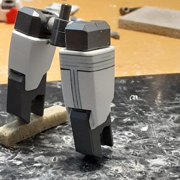 脚部の太さや長さのバランスを調整した0ガンダムの下半身。膝の位置関係から、左右の腿の長さが変わったのがよくわかると思います。 キットのままだと腿は細くて短いので、左右に2mm、上下に5mm延長。股関節の付き位置を1.5mm上げて、ロール部の分割ラインが目立たないように加工。結果的にもともと長い脚が1mm強長くなりましたが、これは腿やアンクルガードの横幅を増やした分、相対的に上下に短く見えてしまうのを防ぐためでもあります。 ↑の「1mm強」の内訳：足首関節で-3ｍｍ、アンクルガード用のジョイントで+1.2ｍｍ、腿の延長で+5ｍｍ、股関節を上げて-1.5ｍｍ 膝関節上部に付いている白い物は、腿の幅増しで空いた分の隙間を埋めるためのプラ板。こういう平面上に薄い板が一段被さったようなデザインが好きなもので。膝を曲げる時にふくらはぎに干渉しないギリギリのラインを狙った位置に貼っています。（4枚目）