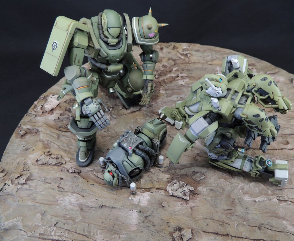 ■胸部の工作 1.0mm厚プラ板を3.0mm幅の帯状にスライスし、両肩に湾曲させて接着しました。プラ板の湾曲は、胸部パーツのカーブに沿うよう、手で曲げて微調整を行っています。キットの胸部を少し削り、積層プラ板を貼り付けてヤスリで六角形に整形しました。 その他、タミヤのパイピングケーブル(外径φ0.5mm/ブラック)2本を瞬間接着剤で貼り合わせ、首元からアンカーまで這わせました。途中のケーブル固定パーツは、エバーグリーン製の「コの字」型プラ材をスライスしたものを貼付けて中にケーブルを通して表現しています。■アンカーの製作 アンカー基部にコトブキヤ製モデリングサポートグッズの丸型の部品を使用しました。筒状の部分は、ザクバズーカ・ザクマシンガン・ヒートホークのパーツ群が収まっている太めのランナーからの削り出しです。