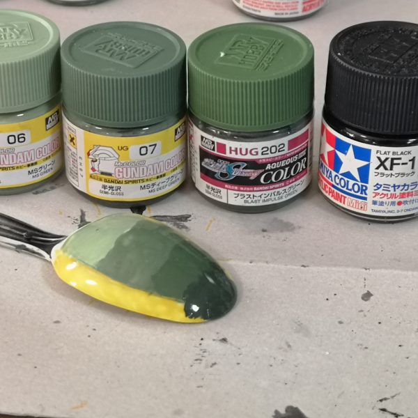 以前、GQザクの塗分けライン同塗分ける？という投稿に付属のシールでマスキングすれば？などと発言したので、責任をもって検証ししました。結果、普通にマスキングテープを細切りにした方がラクだな。との結論に至りました。途中、シールをトレースしてマステを切ったら？とも思ったのですが、曲面がきれいにカットできませんでした。成形色は緑が3種類。シールにあるのはおそらく中間の色。塗分けはラインが入りそうな所に白or黄色を塗っておく、肩のグリーンも。細切り（今回は１ｍｍ）のマステを貼っていく。曲線は自分の直感を信じて・・・スパイクアーマーは１か所一体成型になっているので、一旦切り離す。裏に肉抜きがあるので、そこをガイドに１㎜プラ棒で軸を作る。微妙に角度がついているので最終接着時に注意。マスキングが円形になりますが、黄色いラインの小径ｒが約8ｍｍ、ダイソーのサークルカッターで切れました（メモリが当てにならないので、手持ちのスケールで合わせた方が良い）。ラインの太さのお好みで大径を決めればよいかと思います。肩と腕の黄色いラインは一段下がっているので、最後あとから塗って、はみ出した部分をふき取るか、２段階にマスキングすればどうにかなりそうです。あとはマーキング類ですが、背中の２か所文字らしきものは、なんて書いてあるか解らないので、それっぽいヤツを貼ればヨシっ！！ジオンマークは若干サイズが違いますがガンダムデカールのジオンMS用③が赤白黄灰色の４色で大中小とあるのでそのへんかな？問題は盾の正面にある撃墜マーク？？っぽいのとジオンマークの下の「MAY VICTORY BE WITH US」の文字ですね最後に参考程度に手持ちのガンダムカラーのグリーン系（ラッカーと水性が混じっておりますが）左からラッカーのMSグリーン、MSディープグリーン、水性のﾌﾞﾗｽﾄｲﾝﾊﾟﾙｽｸﾞﾘｰﾝ、←たすブラックです。ん～どうでしょう、長くなりましたが参考になりますかね？（7枚目）