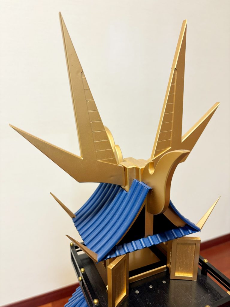 「烈光破空角(れっこうはくうかく)」。烈光頑駄無の兜飾りを模しており、最上階の屋根に突き出ている。単なる飾りではなく、天地城から烈帝城に改装する際に追加された装置である。太陽翼と併用することで、頑駄無軍団が持つ光の力を増大しつつ、闇の性質をもつ攻撃の威力を減退する結界のようなものを展開できる。技術者の中には「あいふぃーるど」と呼ぶ者もいるようだ。という自分設定。太陽翼との併用前提なので、もともと光の力が弱まっている場合にはエネルギー不足で十分な効果は発揮できないかもしれません。作業的には、プラ板が重なる角の部分をトキントキンに尖らせるのに苦労しました。