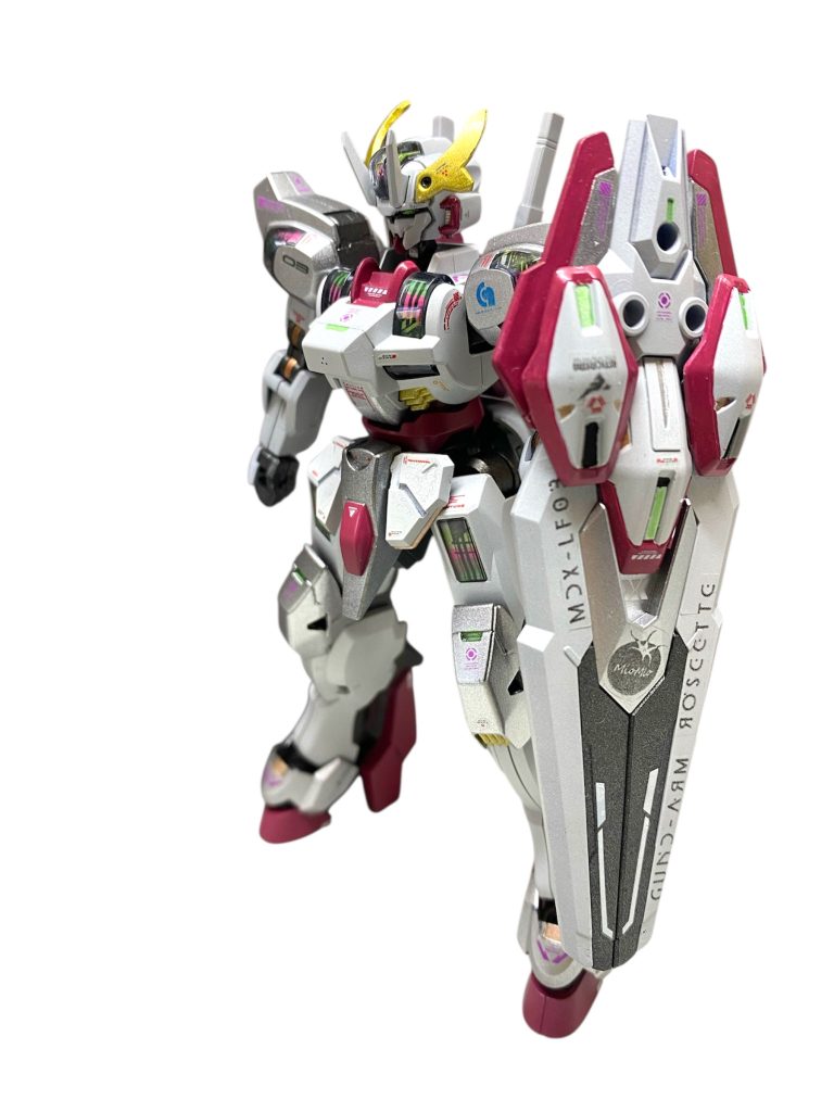 【機体解説】MDX-LF03 ガンダム・ローゼッテは、ミオミオこと株式会社ガンダムCEOミオリネ・レンブランが搭乗するカスタマイズMSである。が、実際に機体を操縦しているのは彼女が身につけているホッツさんの中に居るエリクト・サマヤであり、本機には彼女が初めて操縦したLF-03ガンダム・ルブリスをイメージしたカラーリングが施されている。これまでGUND技術を応用した医療機器の開発のみを行い、MS製造には決して手を出さなかった同社だったが、仮面武闘会への参加が決まった事から、かつて業務提携した経緯を持つジェターク・ヘビーマシーナリーとシンセー開発公社の在庫していた予備パーツをかき集めて急遽、本機が組み上げられた。フレームおよび本体の大部分は、かつてジェターク社が研究開発していたGUND-ARMシュバルゼッテの予備機がベースとなっているが、GUNDフォーマットの要となるシェルユニットや背部フライトユニット、各部アーマーなどはエアリアル系の予備パーツが組み合わせられている。