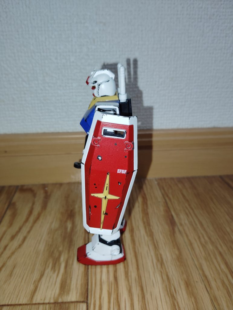 　サイドビューです。　今回は「アムロ・レイの乗ったガンダム」ということで、ウェザリングはどこまでやって良いものか非常に悩んだのですが、ファーストガンダムを見返してみるとなんだかんだでアムロのガンダムが被弾するシーンは多く（特に地上戦）、また、ホワイトベース隊も補給や整備の状況が良いとは言えない有り様だったので、それなりに派手に施しました。　特にシールドは、「ニュータイプに覚醒したアムロとはいえ、普通にシールドで攻撃を防ぐくらいはするだろう」と考え、被弾して塗装だけでなく装甲が削れたことを表現するため、黒鉄色の中心に何ヶ所か銀色を入れてみました。