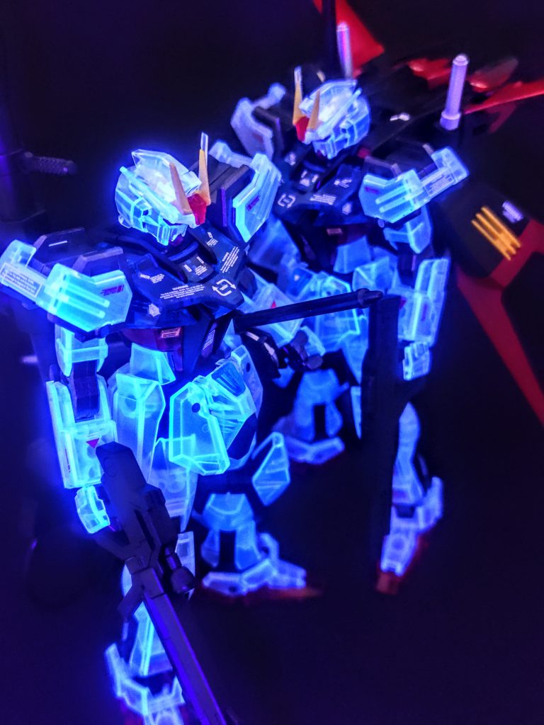 というわけで、今回はせっかくなんで、クリアカラーストライクガンダムを光らせてしまいますよ（笑）。2機光るとこんな感じになります。こっちは前回のスマートな方。一番くじの過去弾にあった、ソリッドクリア、その2つを組み合わせて、出来るだけクリアパーツを使ったものがこれ。どちらも共通して胸の青のパーツはクリアなんで、これを作るとそこだけが余り、残りは通常カラーのランナーパーツが残ります。ようは胸だけクリアのストライクガンダムが余りますよと。