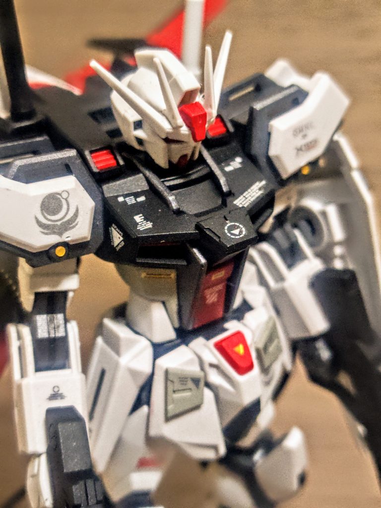 そこから部分的に塗りにくいものはクリップ付きの持ち手棒ではさんで塗装です。ゆえに胸の青を黒に。簡単なデザインチップを見つけたので、それを先につけてまとめて塗装。胸の先端のところですね。コクピットの含まれるパーツはグレー、ここだけマスキングしてあとから赤色を追加。あとはカラー版の通常ストライクガンダムのランナー構成通りに、上半身をランナー塗装です。