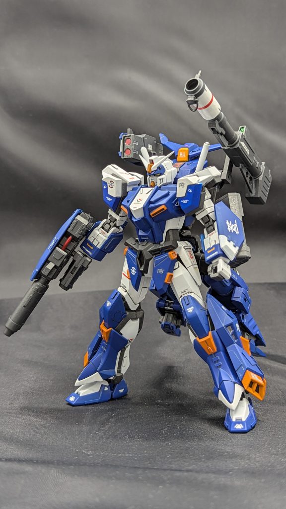 【フロントビュー】原作のアサルトシュラウド系列は腕を動かしたら肩についている武装が軒並み使えないよなぁと思いバックパックに繋ぎました。シルエットはパーフェクトガンダムⅡに寄せつつ、アサルトシュラウドが元はモビル ジンの装備なので、ジンのエッセンスも感じられるようにM66キャニスやM68パルデュスの後継モデルという設定でジャンクのミサイルパーツをチョイスしました。ダブルビームガンはガンダムエース付録のものをディテールアップして使用しています。左腕のバックラーは元々右腕についていたものを切り離し、再接着しています。