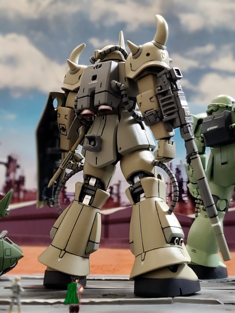 連邦軍のMSが各戦線に姿を表すようになった宇宙世紀0079年10月初旬。オデッサ鉱山基地にYMS-07A-2 グフ・スタンダードカスタムが納入された。新たな愛機となるA2グフを見上げ、その姿に笑みを浮かべるケラーネ将軍。A2グフは近接戦闘特化の装備を排除し標準性能の向上を目指した量産試作機。グフの当初のコンセプトである近接特化装備を取り払い、どの局面でも運用可能な機体へと見直されたオールラウンド型である。その姿はコクピット形状と脚部動力パイプが露出しており、開発ベースとなったプロトタイプ１号機の系譜を感じさせる姿となっていた。両脚部スラスター外側はバーニアスラスターへ変更。これにより高い瞬間機動力の獲得に成功。また左腕マニピュレーターは様々な兵装を可能にするため通常型へ変更。現存するMS装備を全て使用可能にしていた👍️✨こうして汎用性を高めたA2グフは生産数はわずかであったが、各戦線の熟練パイロットに供給されたのである…。