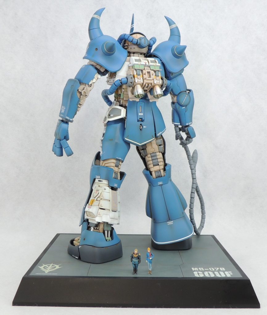 ■台座　キットには台座が付属していないため、サイズ的に丁度良いタミヤのディスプレイベース・スモール(148mm×108mm)を使用しました。格納庫の一部に見立ててパネルラインのスジ彫りを入れ、下地をグレーサフで塗装した後、油彩によるドッティングにより複雑で奥深い色味を出しています。雰囲気としては、ザンジバルの格納庫をイメージしています。使用したデカールは、ジオン公国章はガンダムデカール1/100ギャンから流用し、文字はスジボリ堂のチッピングデカールを使用しました。