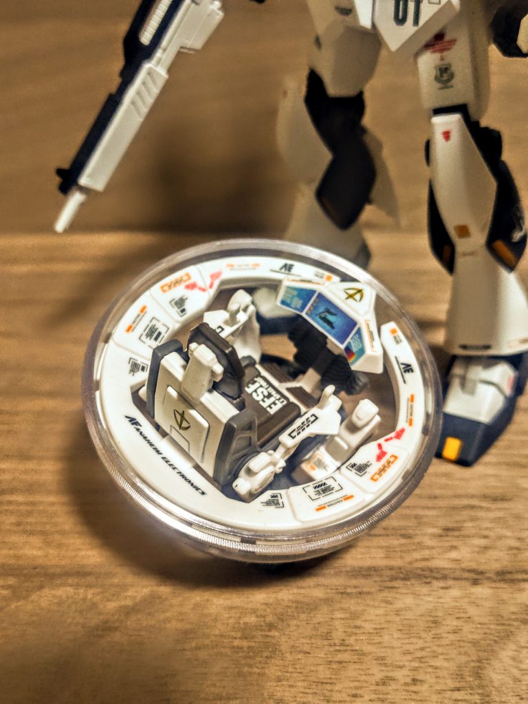 良くできてるんですよね。面白いですし、本当にアイデア賞。ちょっと嬉しいじゃないですか？、カプセルの中にミニチュアコクピットの模型がある。貼ってませんが、そのカプセルに敵の位置やロックオン、ミサイルとか、良く見るあのマーキングがシールになっていて、貼ると透明カプセルが立体的なパネルディスプレイに、って書いてて何を言ってるのかわかりませんね（笑）。ちょっとだけ画像を拝借。