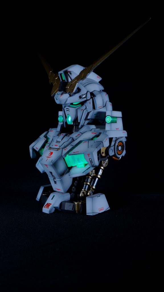 【斜め前】外装の塗装は黒サフの上にMr.Color GX クールホワイトをグラデーションをかけて塗り、スーパースムースクリアーで仕上げています。アンテナの金はいつものスターブライトゴールドとスターブライトシャンパンゴールドを調色したものになります。サイコフレームは胸部については、パーツの裏側にシルバーを塗り、表面にガイアノール　プリズム パステル ミントグリーンブルーをクリアーと混ぜて薄く塗り、その上に蛍光グリーンを塗っています。そのため、サイコフレームはUVライトで光ります。(zaku-kao5)