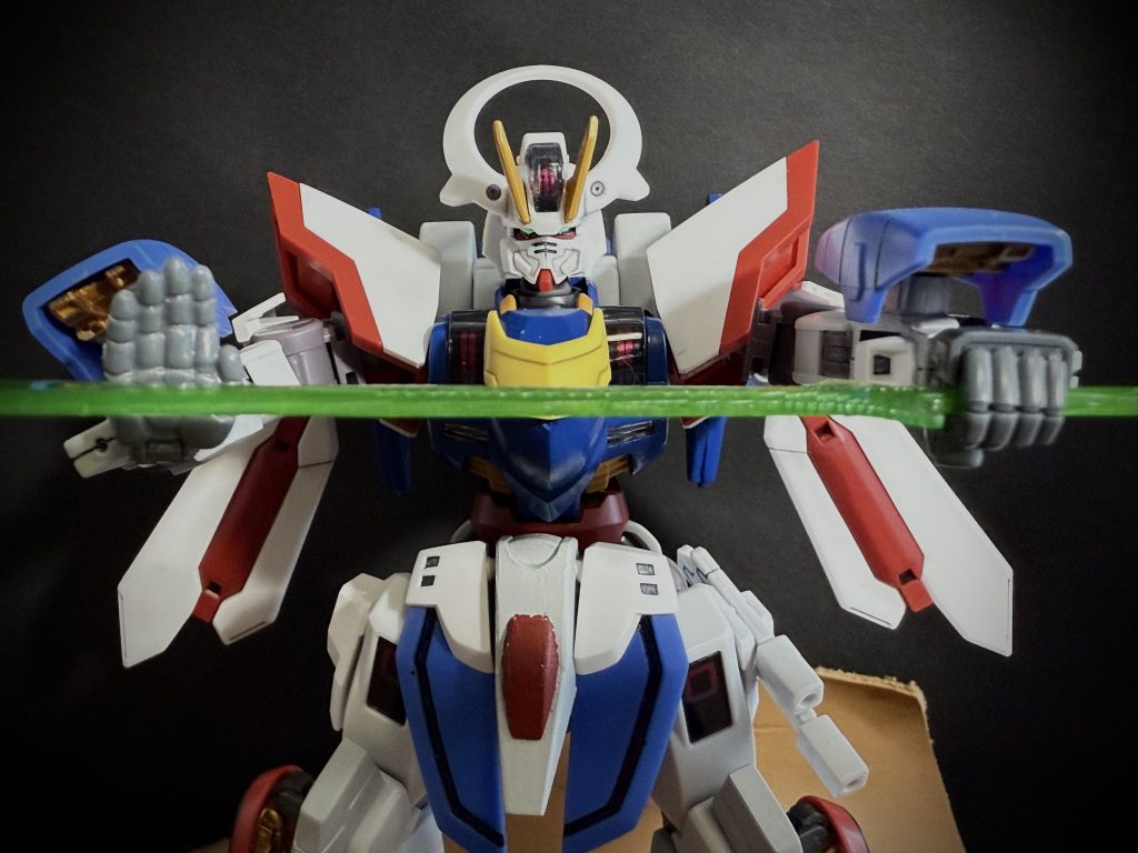 決闘　其の一パイロット　ヴォルジュ•ド•サンドMS &nbsp; ローゼンエリス「克州土門ッ！…貴方は我が家名を汚しました！」　目の前のMSがそう言うのを土門は見据える。ミカエリスベースの青と銀の機体、装甲の大部分に華美な、薔薇を思わせる装飾（エングレービング）が施された中世の騎士といった佇まいのMSだ。その背にやや大きめのプロペラントタンクと思われるユニットが華美な機体にそぐわない、どこか不気味な雰囲気出している。両の足をピシリと揃え、右手を腰の後ろに、左手でビームレイピアの柄を頭部、顔の前に持ってきている構えには一部の隙も無い。　コイツ、出来る。そう思った瞬間、土門の視界、モニターから青銀のミカエリス、ローゼンエリスの姿が消える。次の瞬間、シャイニングガンダムの頭部にビームレイピアを突き刺さんと、腕を伸ばしたローゼンエリスの姿。寸での所で鋭い突きを躱す土門。…速いッ！だが、土門もまた武術の達人である。素早く身を翻し、カウンターとなる一撃を叩き込まんと、回し蹴りを放つが空を切る。…見ると、最初の位置、先程と全く同じ構えのローゼンエリスの姿が目に入る。…まさか、瞬間移動。そう困惑する土門に対し、ローゼンエリスは容赦なく鋭い突きを放ってくる。数十メートルの距離をものともしない攻撃。しかし、土門は気付く、ローゼンエリスの姿が消えているのではなく、凄まじいまでの加速力でもって消えている様に見える事に。「…かつて、グラスレー寮に、機体性能を加速力一点に振り切った漆黒のハインドリーを操るサムライがいたと。…私のローゼンエリスもそうですッ！」　土門が自分の機体性能に気付き、動きが変わった事に対し、ヴォルジュが言う。一方、土門は防戦一方だ。なぜなら、ローゼンエリスが突きを放つ際、その踏み込みの一歩一歩の距離が微妙に違い、突き出す際のビームレイピアのビームの刃の長さも一撃ごとに違うのだ。単調にならざるを得ない突きの連続使用、本来ならば大きな隙が目立つはずだ。だが、踏み込みの距離、繰り出す刃の長さを変える事で、隙のタイミングを意図的に変える事で、逆に隙が少なくなっている。…一撃一撃の隙のタイミングが違えば、カウンターを当てることも出来ない。…しかし、土門もまた、格闘家の端くれ、矢継ぎ早の攻撃を確実に防御しながら打開策を出す。　突如、防戦一方でその場にとどまっていたシャイニングガンダムがローゼンエリスにぶつかる様にダッシュすると、今まさにビームレイピアを突き出さんとするローゼンエリスの手首をガシリと掴んだのだ。「攻撃が見えないのならば、攻撃の前に止めれば良いッ！」　土門が叫ぶ！土門の格闘家としての動体視力、土門の動きをそのままトレースするパーメットトレースシステムあっての芸当である。その後の何度かの攻撃を止められ思わず距離を取ってしまうローゼンエリス。だが、再びピシリと構えたままヴォルジュは意に介せず言う。「…そうでした。貴方のスピードを忘れていました。であれば、貴方のそのスピードを奪えば、…どうなるでしょう」　ヴォルジュが不敵に笑うと同時に、ローゼンエリスの背後、プロペラントタンクだと思われていた筒状のユニットが立ち上がると、先端が展開、中から薔薇の花が咲く。ローゼンエリスがその背に二輪の薔薇を咲かせた様に見える。「ローゼンビットッ！」　そうヴォルジュが叫ぶと同時に先端から薔薇の花が外れ、宙に浮くとその花芯の砲塔からビームを放つ。「がっかりだなッ！ヴォルジュ•ド•サンド！たかだかビーム砲如きで俺を止められるとでも思ったのかッ！」　しかし、シャイニングガンダムを突撃させた土門の叫びは、次に起きた出来事に打ち消される。宙に浮く二輪の薔薇の花びらが散ると、その散った花びら一枚一枚の先端から赤いレーザーが放たれたのだ。そのレーザーはあらゆる方向から網の様に放たれ、シャイニングガンダムを貫く。「…ローゼススクリーマー。…ペイル社の『コラキ』を改良させていただきました」　薔薇の花びらから放たれる行動不能（スタン）効果の電磁ビームがシャイニングガンダムの動きを止めていく。全身を突き刺すような痛みが土門を襲う。身動きが取れず、声すら出せない土門の耳に、ヴォルジュの叫ぶ声だけが聞こえる。「覚悟なさい！克州土門ッ！…ローゼスハリケーンッ！！」　動きの取れないシャイニングガンダムに、無数の剣尖とビームが襲い掛かる。