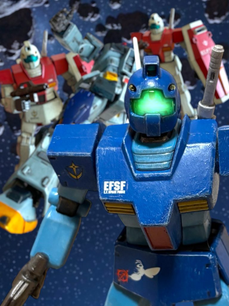 　敵は、そのままマイセンにぎりぎりまで近づき、ゴツンとヘルメットのバイザーを押し当てた。共振による直接会話をするつもりらしい。『大尉！』　ローワンの慌てた声が、ヘルメットのスピーカーに響いたが、大丈夫だ、と低く応えた。小銃の銃口は、しっかり相手の腹に押し当てている。『……要求どおり、超えてみせたぞ。満足か、爺ィ。』　若い敵兵は、まっすぐな瞳を向けて言った。「ああ、ありがとうよ。」　心からの、礼を述べる。おかげで、膿を出しきれた、と言うと少し違う気がするが、とにかく、この若者のおかげで、何かが変わった気がする。今日の宇宙は、どこか、青く、澄んでいる。そんな気がした。『闘いには勝ったが、戦には敗けた。俺たちはもうこれ以上、戦えない。』　淡々と感情を殺したように言う姿は、現状を受け入れいるような清廉さを感じた。やはり、戦士として、この男には好感が持てると思った。「潔いな。」　素直に賛辞を口にしたが、敵は、応えなかった。その瞳に、深い哀しみの色が宿るのを、マイセンは見た。『俺は降りる。もう戦わない。仲間と、一緒に帰る。』　数秒の沈黙の後、若い敵兵は呟いた。その目は、マイセンをじっと見つめていたが、もっと、ずっと遠くを見ているようだった。「帰る、だと……？」　どこへ、帰ると言うのだ。ヤツらの基地も、投降しているか、全滅しているはずだ。仲間と一緒に、と言うが、出撃してきたMSは、コイツの機体を除いて、もう戦場には残っていない。『あいつらと一緒ならどこだって帰る場所になる。』　澄んだ瞳の視線と共に、明確な意志を宿した声が返ってくる。　もしかして、コイツの言う”仲間”には、喪われた者の魂も含まれているのではないか。マイセンは、そんなことを想像した。　おそらく、互いに、愛する者を喪った。憎しみ合いながらも、その胸の内に燻り続ける熱を、ぶつけ合うような戦い方をした。マイセンは、目の前の若者に、勝手に、自分を重ねている。それは、この若者に、救いを求めてしまっているのかもしれない。馬鹿げたことかもしれない。だが、その澄んだ瞳の色に、マイセンは、もう２度と抱くことのできない、娘と妻の面影さえ、見たような気がしたのだ。（アリス……アイリーン……わたしも……。）　帰る場所が、あるのだろうかーーこの、若者のようにーー？　お前たちが、待っていてくれた、あの家のような……帰る場所が……？　思うと、つい、唇が動いた。「ならば……わたしも……帰ることが……？」　ピクリと、若者の眉が動いた気がしたが、マイセンの呟きには返事はなかった。そもそも、これは、彼への問い掛けであったのか、マイセンにすら、分からない。ただ、続いた沈黙に、その応えは、お前が探せ、という彼の意志が含まれているかのように感じられただけだ。　しばらくして、若者が口を開いた。『投降する。お前の要求を飲んだんだ。今度は、勝った俺の要求を、お前が飲め。』投降する者の態度とは思えないが、その太々しさを、マイセンは気に入った。やはり、気骨がある。「言ってみろ。」『南極条約に基づいた、捕虜としての身柄の保証を求める。』バカが、とマイセンは笑った。「そんなことは、当たり前だ。」　だが、この若者は過酷な戦場の、最前線にいたのだ。その当たり前を、改めて要求せねばならないような、悲惨な光景を目の当たりにしてきたのかもしれない。『分かっている。だが、戦いで血を滾らせた連中のやることなど、信用できん。』　やはりだ。『約束したんだ、俺は。生き延びなきゃいけない。だから——……。』　若者は、一瞬、瞳を揺らしてから言葉を続けた。『俺が無事生き延びて、捕虜返還が果たされるまで、お前が責任を持って面倒を見ろ。俺の仲間たちもだ。虐待や、理不尽な扱いは、お前が絶対にさせるな。』　なるほど、そういうことか。『紀章を見た。さっきの通信も聞いた。大尉だろう。なら、できるな。』「ああ、良いだろう。」　マイセンは、ニヤリと笑った。（あなたが、あの子の父親がわりに、なってあげて。）　幻に見た、妻の声が蘇る。「デニー・マイセン・ライオス大尉だ。わたしが、全権限をもって、ここまでの健闘を果たした諸君らの身柄を保証することを約束しよう。」　マイセンが言うのを聞いて、５秒、ジオンの若者はマイセンの瞳をじっと見つめた。そして、若く、張りのある声で言った。『マイロ・アンダーソン少尉だ。ガンダムを倒した男の名だ。たとえ記録から消されても、お前は覚えておけ。』言って、マイロ・アンダーソンは両手を揃えて差し出した。マイセンは、その両手をしっかりと拘束し、彼を収容した。～～～～～～～～～～～～～～～